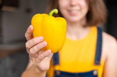 Gülümseyen bir kızın arka planına karşı dişi elinde sarı biber, sağlıklı bir sebzeye yakın plan..