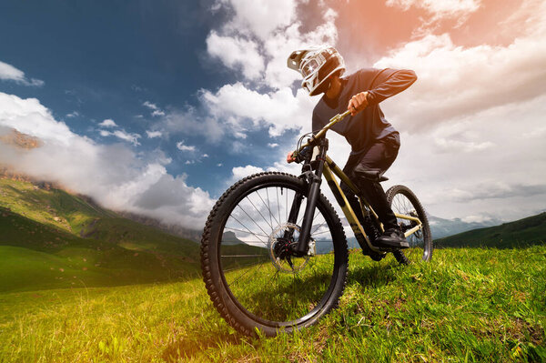 Professional cyclist speeds down a rocky path among grass. Extreme sport in the mountains.