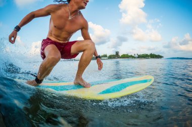 Genç sörfçü gün doğumunda okyanusta tropikal dalgalarda sörf yapıyor.