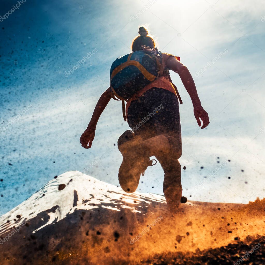 Woman athlete runs on a dirty and dusty ground with volcano on the background. Trail running athlete working out in the mountains