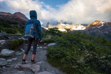 Yürüyüşçü patikada durur ve bulutlarla kaplı dağları sever.