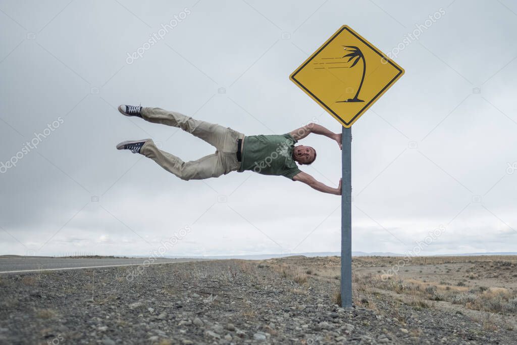 Man having fun with road sign set on the patagonian road in latitudes of Roaring Forties famous by its strong winds. Argentina