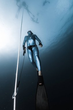 Freediver, elinde emniyet tasmasıyla ip boyunca bir derinlikten yükselir. Öğrenciler deniz yüzeyinde beklerken fredive eğitmeni serbest dalış noktası hazırlıyor.