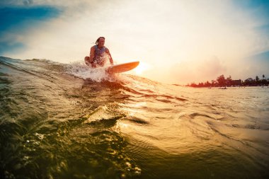 Genç sörfçü gün batımında dalgalara biner.