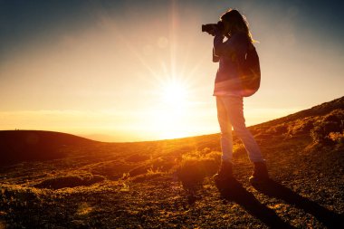 Sırt çantalı kadın yürüyüşçü, altın saat boyunca dağlardaki manzaranın fotoğrafını çeker.