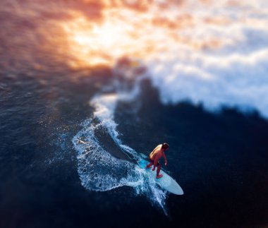 Aerial view of the young man surfs the wave at sunset. Tilt shift effect applied clipart