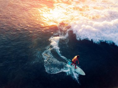 Gün batımında dalgada sörf yapan genç adamın hava görüntüsü.