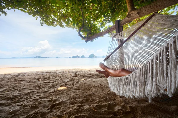 地平線に熱帯の島がある砂浜のハンモックでリラックスしている若い女性 — ストック写真