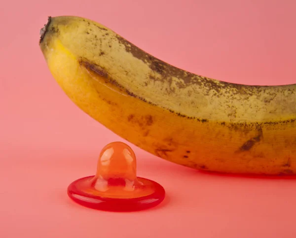 ピンクの背景のバナナと赤のコンドーム — ストック写真