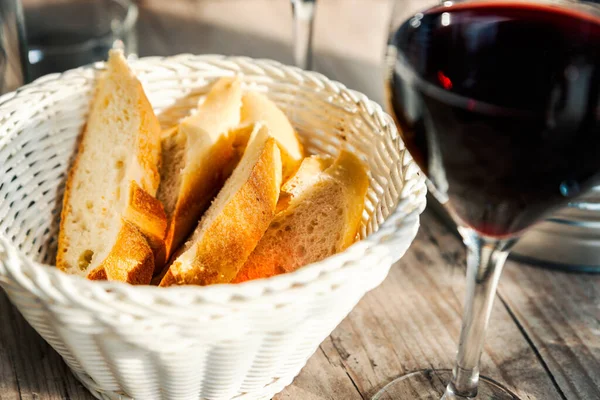 Baguette slices in basket and a glass of red wine — Stock Photo, Image