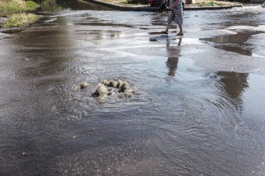 Yol kanalizasyon kapağından su akar. Lağım kanalizasyonu. Kanalizasyon sistemi kazası. Kirli lağım suyu yolda akar. Ambar çeşmesinden su akar