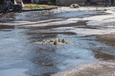 Yol kanalizasyon kapağından su akar. Lağım kanalizasyonu. Kanalizasyon sistemi kazası. Kirli lağım suyu yolda akar. Ambar çeşmesinden su akar