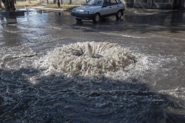 Yol kanalizasyon kapağından su akar. Lağım kanalizasyonu. Kanalizasyon sistemi kazası. Kirli lağım suyu yolda akar. Ambar çeşmesinden su akar