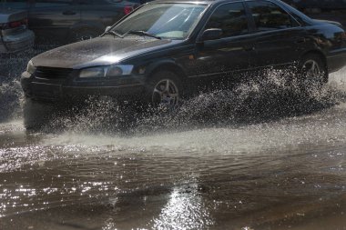 Yağmur fırtına tarafından neden olduğu sel sırasında su dolu bir yolda araba sürmek. Arabalar sokaklarda sel su üzerinde yüzer. Sıçramak üstünde belgili tanımlık makine. Büyük bir su birikintisi olan sular altında şehir yol