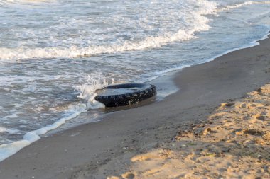 Eski siyah kauçuk lastik beach, çevre kirliliği kavramı, seçici odak, renk tonlu resim solda. Eski lastik plajda mavi su atılır. Kirliliğini ve çöplükte deniz ve plaj