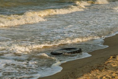 Eski siyah kauçuk lastik beach, çevre kirliliği kavramı, seçici odak, renk tonlu resim solda. Eski lastik plajda mavi su atılır. Kirliliğini ve çöplükte deniz ve plaj