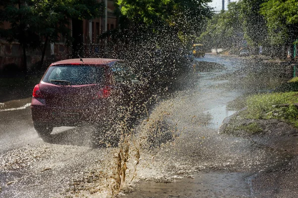 在暴雨引起的水灾中 驾驶汽车行驶在洪水泛滥的路上 汽车漂浮在水面上 淹没了街道 在机器上飞溅 洪水泛滥的城市道路与一个大水坑 — 图库照片