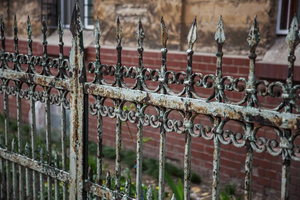 Old forged iron cast iron fence with sharp spears and cracked paint from time to time. White dirty abandoned fence that broke through the years of neglect.