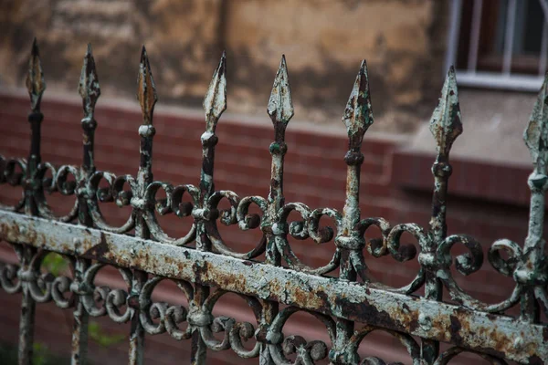 Old forged iron cast iron fence with sharp spears and cracked paint from time to time. White dirty abandoned fence that broke through the years of neglect.