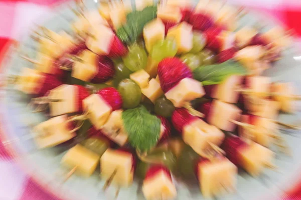 Bright abstract dish background with grapes, strawberries and cheese. Unusual bright abstract background of cheese with grapes on sword-toothpick for restaurant. Selective not deep focus, blur