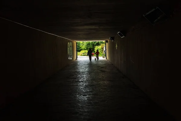 Long stone tunnel. Light at the end of the tunnel at the destination. Silhouettes in a tunnel against the background of light at the end of the road. Gloomy creepy picture as background for design.