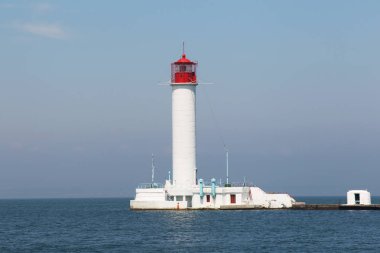 Deniz gökyüzü altında deniz feneri. Limanın ortasında bir beyaz deniz deniz feneri gece ve ışık ile sisli zaman gemilerin yol gösteriyor.