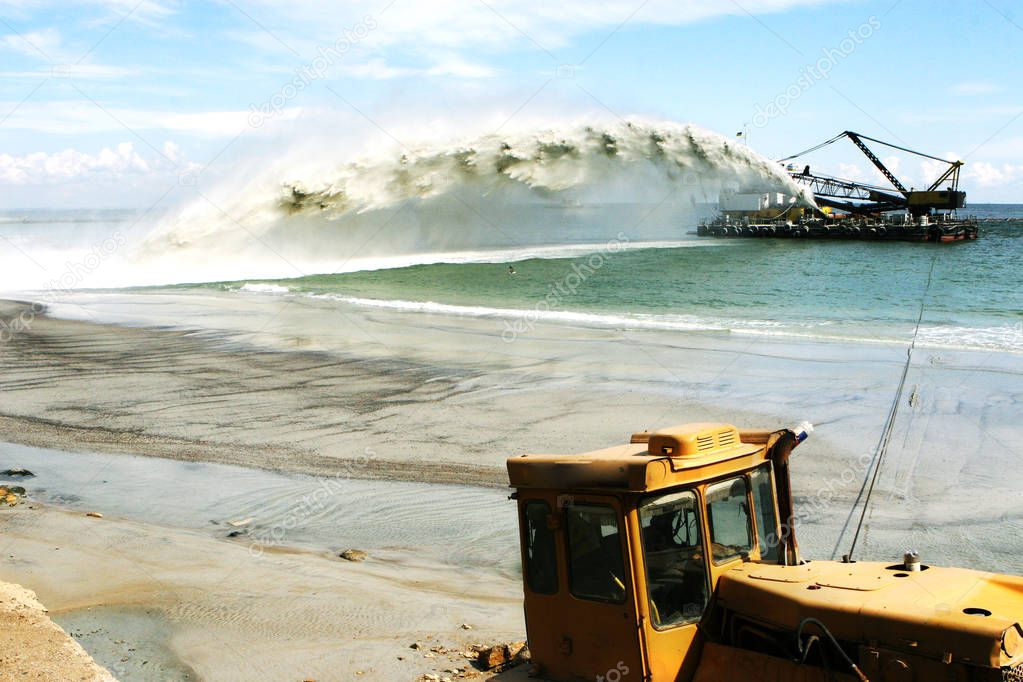 Work dredger dredging with sand washing on beaches. Special dredging hose for sand to create new land. Sand washing on sea beaches. Dredging, washing out sand on beach during construction sea terminal