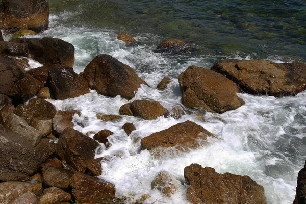 Beautiful sea waves are broken on the rocks of the rocky coast. Bright landscape view as a background for advertising of summer travel, rest on the sea, ocean. Sea view of waves crashing on a rock