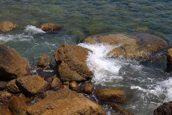 Beautiful sea waves are broken on the rocks of the rocky coast. Bright landscape view as a background for advertising of summer travel, rest on the sea, ocean. Sea view of waves crashing on a rock