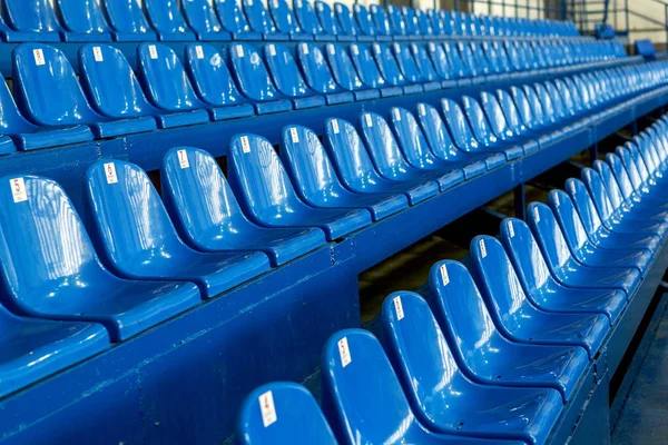 Blank old plastic chairs in the gym. Number of empty seats in a small sports complex. New Rows of plastic seats for fans. Shallow depth of field perspective, soft focus