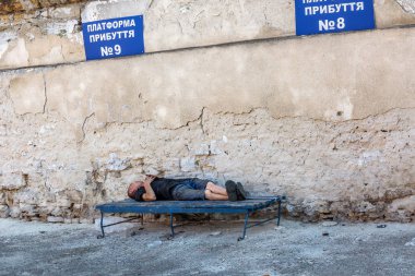 Odessa, Ukrayna - 9 Ağustos 2014: Evsiz uyur bir bankta otobüste soğuk bahar gününde. Başlık: Varış platformu. Fakir bir ülke Ukrayna - Avrupa Birliği'nde aday