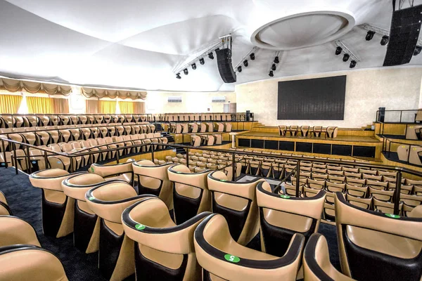 Bright interior of a modern concert hall with a stage and rows of comfortable leather chairs, a stage and acoustic amplification system under natural light, prepared for presentation