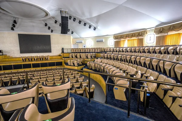 Bright interior of a modern concert hall with a stage and rows of comfortable leather chairs, a stage and acoustic amplification system under natural light, prepared for presentation