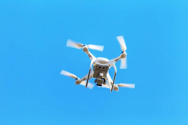 Quadrocopter unmanned camera hovers in bright blue sky above city on background of urban buildings. Modern technology photo and video shooting bird\'s-eye view. Professional Carbon drone with GPS