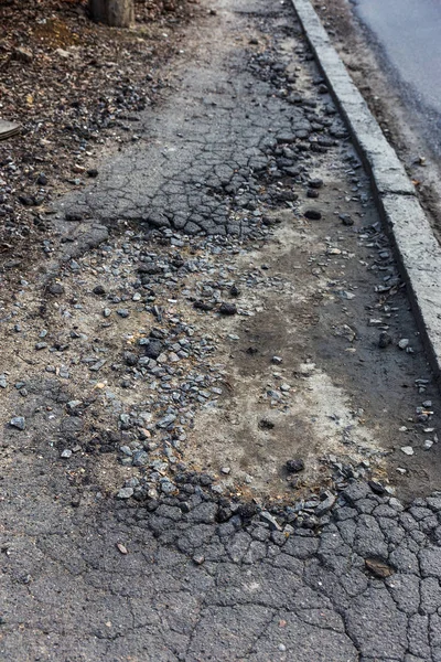 Bad road, damaged by rain and snow, needs repair. Broken asphalt coating leads to pothole, dangerous for vehicles and pedestrians. Bad emergency road. Dangerous road.  Destruction of roads, large cracks