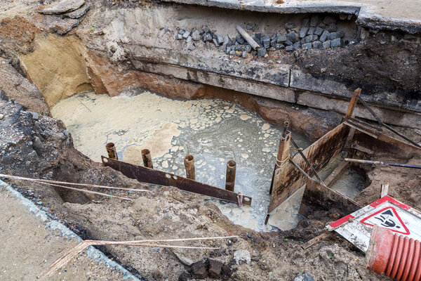 Вырыл глубокие траншеи инженерных городских систем. Сигнализация городской канализации и отопления. Траншею заполняет ржавая грязная вода, извергающаяся из трубопровода. Ремонт подземных сооружений
