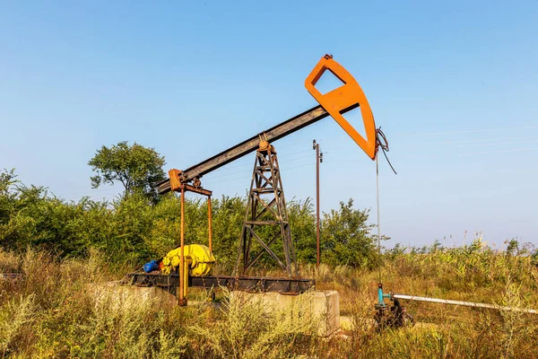 A small private oil derrick pumps oil on the field. The old handicraft oil rig in the background of the creative industrial design. Illegal development of minerals. Bulgaria Tyulenovo, 2016