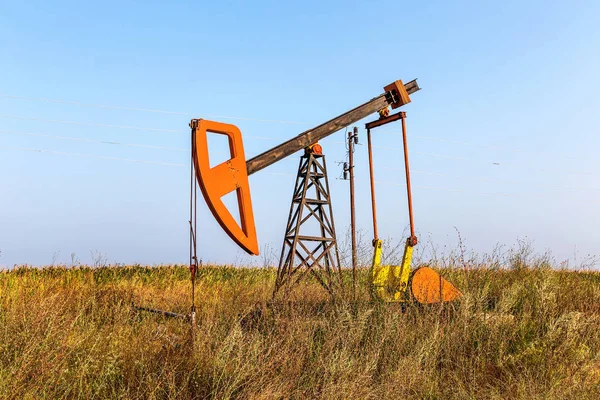 A small private oil derrick pumps oil on the field. The old handicraft oil rig in the background of the creative industrial design. Illegal development of minerals. Bulgaria Tyulenovo, 2016