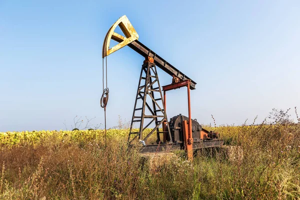 A small private oil derrick pumps oil on the field. The old handicraft oil rig in the background of the creative industrial design. Illegal development of minerals. Bulgaria Tyulenovo, 2016