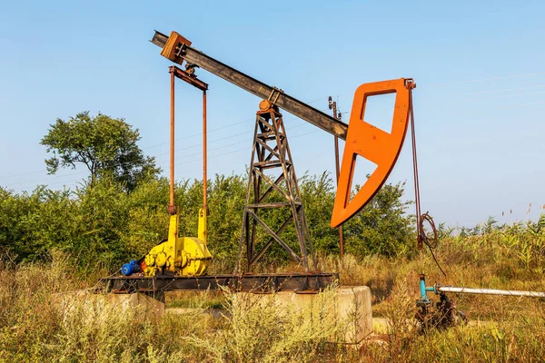 A small private oil derrick pumps oil on the field. The old handicraft oil rig in the background of the creative industrial design. Illegal development of minerals. Bulgaria Tyulenovo, 2016