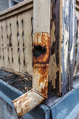 Rusty eski evi yıkmaya çalışıyor. Pas tutmuş eski bir borunun bir parçası. Metalin erozyonunda delik olan eski çürük bir drenaj borusu. Kırık kanal.