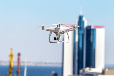 Kentsel binaların zemin üzerine şehir üzerinde parlak mavi gökyüzünde Quadrocopter insansız kamera hovers. Modern teknoloji fotoğraf ve video çekim kuşbakışı. Profesyonel karbon drone ile Gps