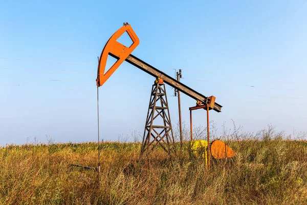 A small private oil derrick pumps oil on the field. The old handicraft oil rig in the background of the creative industrial design. Illegal development of minerals. Bulgaria Tyulenovo, 2016