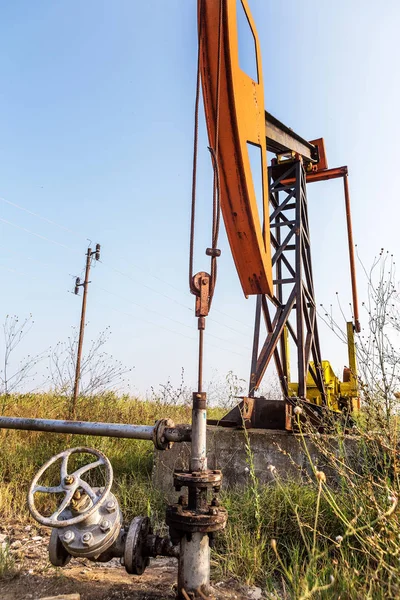 A small private oil derrick pumps oil on the field. The old handicraft oil rig in the background of the creative industrial design. Illegal development of minerals. Bulgaria Tyulenovo, 2016