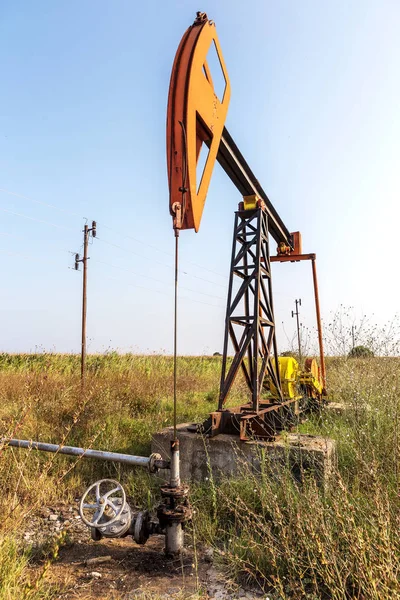 A small private oil derrick pumps oil on the field. The old handicraft oil rig in the background of the creative industrial design. Illegal development of minerals. Bulgaria Tyulenovo, 2016