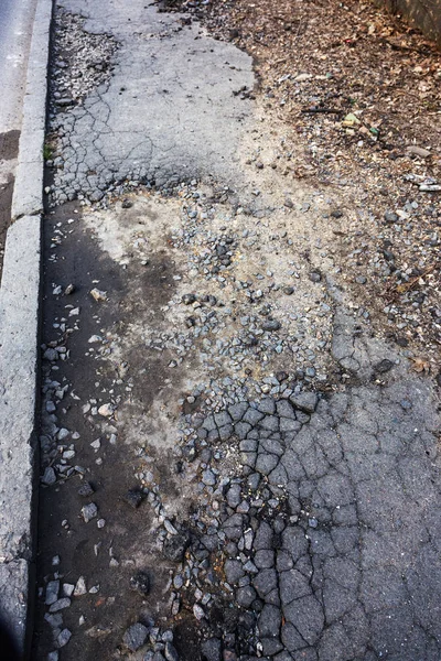 Bad road, damaged by rain and snow, needs repair. Broken asphalt coating leads to pothole, dangerous for vehicles and pedestrians. Bad emergency road. Dangerous road.  Destruction of roads, large cracks