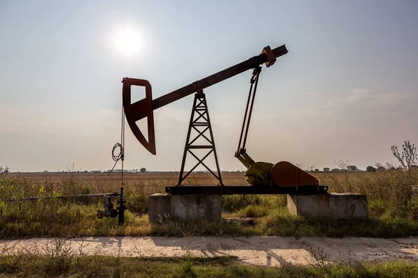 A small private oil derrick pumps oil on the field. The old handicraft oil rig in the background of the creative industrial design. Illegal development of minerals. Bulgaria Tyulenovo, 2016