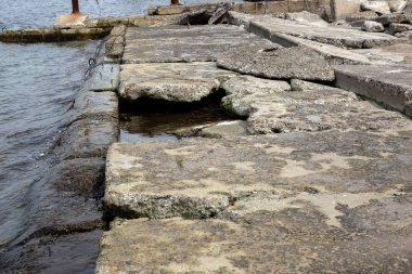 Kıyı beton koruyucu yapı yok. Döşeme blokları arasında büyük derin çatlaklar shore dalga deniz etkisinin erozyon korumak. Beton takviye sahil korumaya ile büyük parçalar