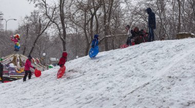 Odessa, Ukrayna - 24 Şubat 2018: Güçlü kar yağışı, şehrin sokaklarında siklon. Mutlu çocuk bir kızak dağdan binmek. Kar yağışı, frost. Kış aylarında bir eğlence parkı. Çocuk iyi eğlenceler