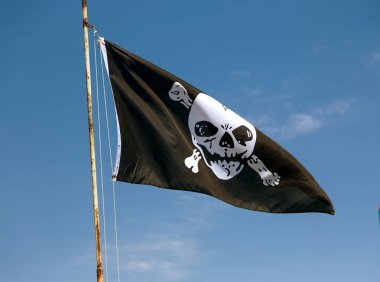 kafatası korsanlar sembolü olarak tasvir eden bayrak parçası. Jolly Roger / kafatası ve kemiklerin korsan bayrak yırtık içinde rüzgara karşı mavi gökyüzü. Gökyüzü karşı rüzgarda üfleme neşeli Roger veya korsan bayrağı